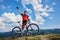 Happy professional sportsman cyclist standing with cross country bicycle on a hill, rasing hand