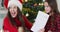 Happy and proud caucasian mother wearing santa hat, looking at her daughter diploma
