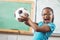 Happy pupil holding football in a classroom