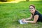 Happy red-haired girl in glasses lies on the lawn in the park and types on the laptop keyboard. Young caucasian female