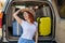 Happy red-haired woman in a cowboy hat and sunglasses going on a car trip around the country. Girl sitting in the trunk