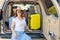 Happy red-haired woman in a cowboy hat and sunglasses going on a car trip around the country. Girl sitting in the trunk