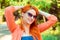 Happy red head woman relaxing hands on head with sunglasses, looking at you camera outdoors park green trees background
