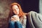 Happy redhead woman relaxing at home in cozy winter or autumn weekend with book and cup of hot tea, sitting in soft chair