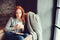 Happy redhead woman relaxing at home in cozy winter or autumn weekend with book and cup of hot tea, sitting in soft chair