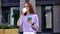 Happy redhead young woman is using phone on city street on background of office building.