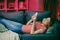 Happy relaxed girl holding smart phone using mobile apps watching funny video laughing lying on couch, smiling lazy