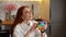 Happy relaxed redhead young woman pushing colorful iridescent soft silicone bubbles sitting sitting at table in light