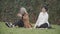Happy relaxed senior and young woman sitting in park playing with dog. Positive Caucasian mother and daughter resting