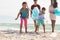 Happy responsible multiracial family collecting plastic garbage from sand at beach on sunny day