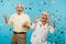 happy retired husband and wife gesturing near falling confetti on blue.