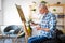 Happy retired man painting on canvas for fun at home