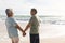 Happy retired multiracial senior couple holding hands while looking at each other on sunny beach