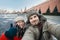 Happy romantic couple of tourists in the winter in warm clothes and hats makes self-portrait selfie in front of the Kremlin on Red