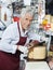 Happy Salesman Slicing Whole Cheese With Knife In Shop