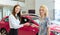 Happy saleswoman handing over car keys to female owner of new car
