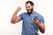 Happy satisfied man with beard in blue shirt holding smartphone and smiling making yes gesture, celebrating online lottery or