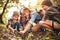 Happy school children boys and girls with backpacks making bonfire with magnifying glass in forest