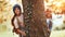 Happy school girls hugging tree in forest and smiling at camera during camping activity in nature