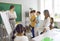 Happy school teacher uses classroom white board while making presentation for children