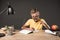 happy schoolboy in eyeglass pointing by finger and doing homework at table with lamp books colour pencils and textbook on grey