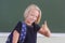 Happy schoolgirl with backpack showing thumb up in a classroom near green chalkboard. The child likes to learn. Back to school.