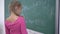 Happy schoolgirl with chalk solves examples on mathematics on school green blackboard during a lesson in class, primary