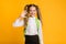 Happy Schoolgirl Waving Hand Smiling To Camera On Yellow Background