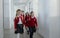 Happy schoolgrirl with Down syndrome in uniform holding hands with her classmate walking in scool corridor with