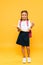 happy schoolkid holding books and showing thumb up on orange .