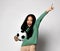 Happy screaming Asian kid girl holding soccer football ball in one hand and the other hand up, showing one, first sign