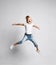 Happy screaming kid girl in blue jeans and white t-shirt is jumping with her arms up spread having fun on white