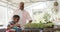 Happy senior african american grandfather and grandson tending to plants in greenhouse, slow motion