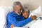 Happy senior biracial couple lying in bed embracing at home