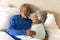 Happy senior biracial couple lying in bed and embracing at home