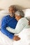 Happy senior biracial couple lying in bed and embracing at home