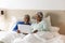 Happy senior biracial couple lying in bed using laptop at home