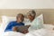 Happy senior biracial couple lying in bed using tablet at home