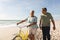 Happy senior biracial woman wheeling bicycle talking with man at beach against sky on sunny day