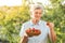 Happy senior caucasian woman picking up strawberries in the garden during the sunset or sunrise. Elderly lady farmer with grey