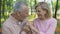 Happy senior couple embraces in park, man kisses wife hands, love until old age