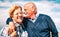Happy senior couple in love enjoying time together - Joyful elderly lifestyle and retirement concept with man whispering on woman