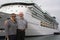 Happy Senior Couple Posing In Front of A Large DockedPassenger Cruise Ship.