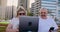 Happy senior couple sitting on a bench in the summer in a modern city with a laptop on the background of skyscrapers