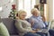 Happy senior couple sitting on couch at home, video calling family and waving hands