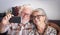 Happy senior couple with white hair and glasses in video call with family with smart phone - active retired elderly people social