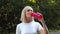 Happy senior lady drinking water from pink sport bottle and smiling outdoors, tracking shot, slow motion