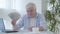 Happy senior man sitting at the table holding pack of dollars and smiling at camera. Portrait of satisfied mid-adult