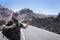 Happy senior man white hair in middle of the road with backpack traveling in mountain volcanic landscape in Tenerife enjoying