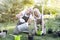 Happy senior married couple taking care of plants and watering pots, sitting in the garden. Retirement activity